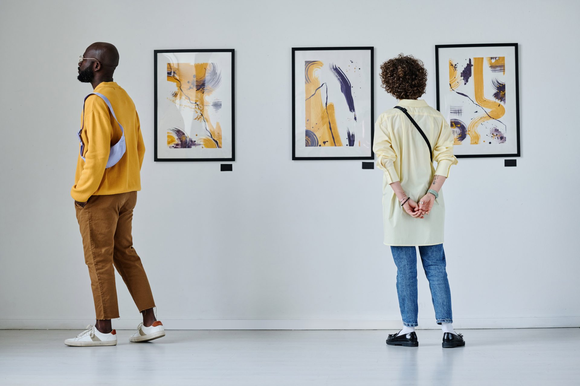 Duas pessoas observando obras emolduradas em uma galeria de paredes brancas